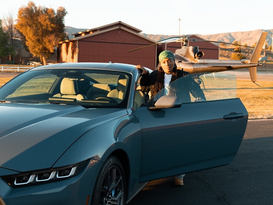 Dee Bryant standing near the open driver-side door of a parked 2024 Ford Mustang® coupe