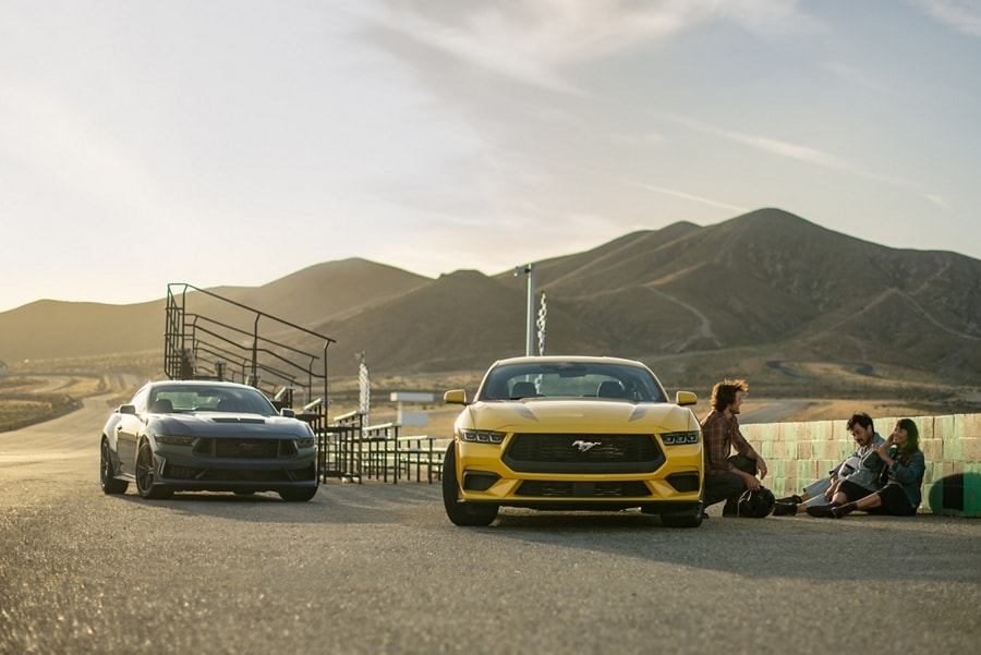 Two 2024 Ford Mustang® coupes parked near a racecourse with three people nearby