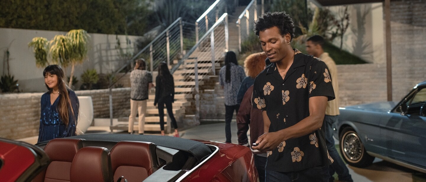 2024 Mustang® GT convertible and a first-gen Mustang coupe parked in a driveway with people nearby