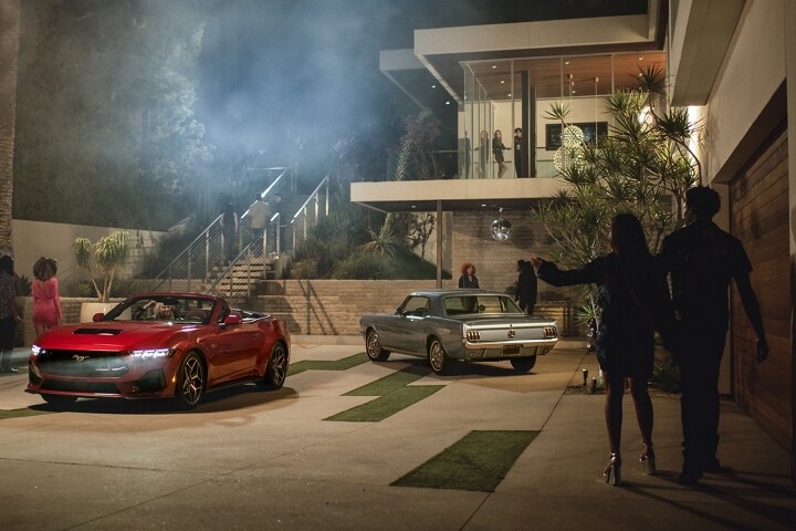 2024 Mustang® GT convertible in Rapid Red Metallic Tinted Clearcoat and first-gen Mustang coupe by people