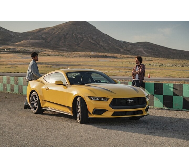 2024 Ford Mustang® EcoBoost® model with available Wheel and Stripe package parked on a racecourse near people