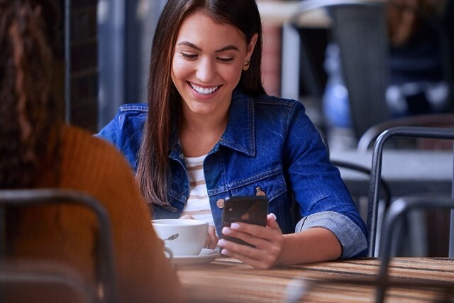 Two people sitting at a table with one using a smartphone