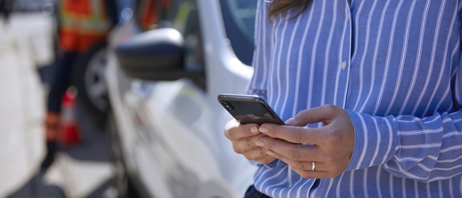 Person using a smartphone while a service tech repairs their tire in the background