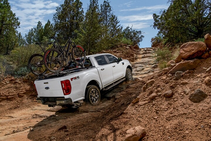 2021 Ford Ranger in Oxford White going up dirt and rock covered path shown with optional bed mounted rack accessory