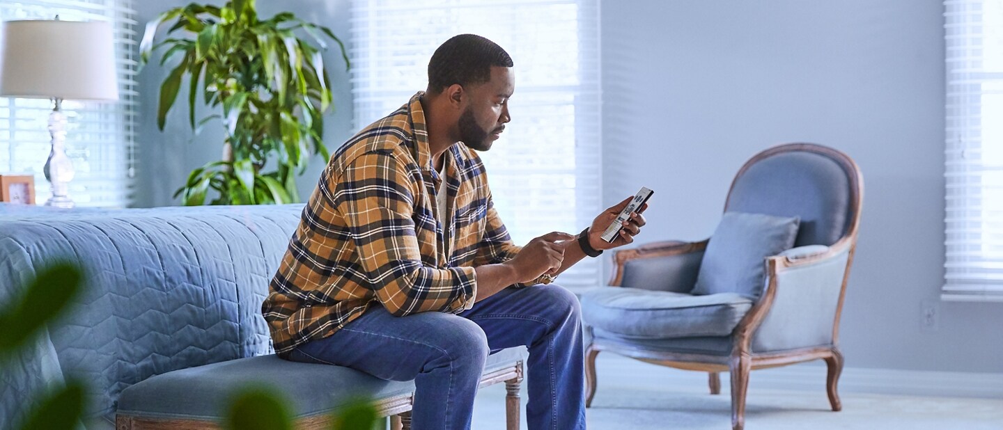 Un hombre sentado en su hogar, interactuando con su smartphone