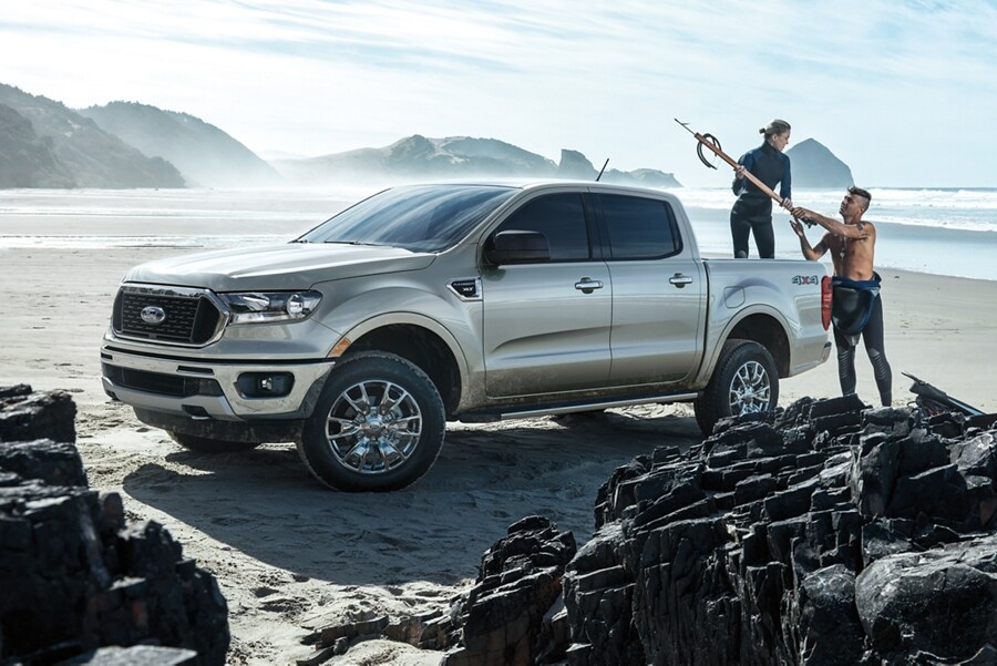 2022 Ford Ranger parked on a rocky beach with surfers loading gear into the box