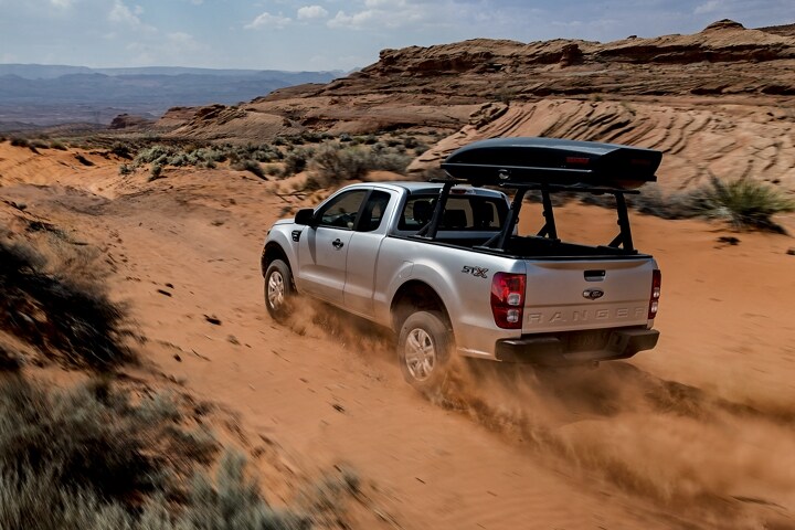 Ford Ranger 2023 subiendo una colina en el desierto con accesorio de rieles opcional montado en la plataforma