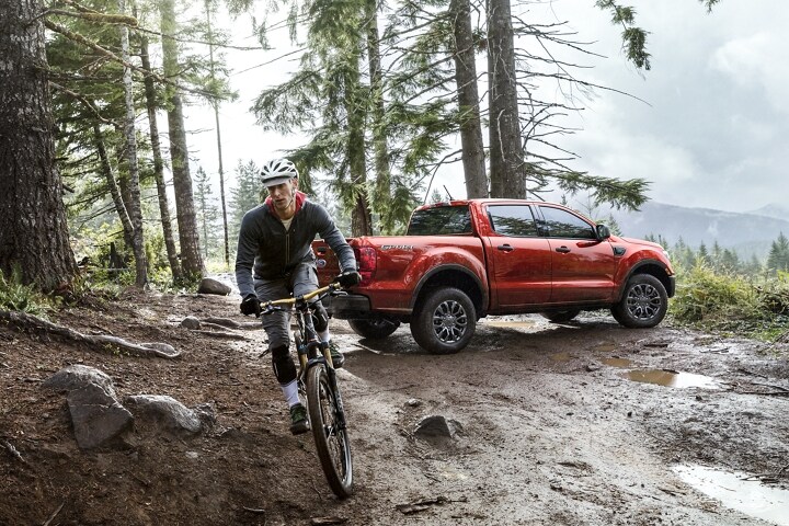 Una Ford Ranger® 2023 en Hot Hepper Metallic estacionada en un bosque y un ciclista que se aleja