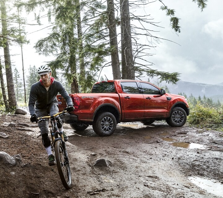 Una Ford Ranger® 2023 en Hot Hepper Metallic estacionada en un bosque y un ciclista que se aleja