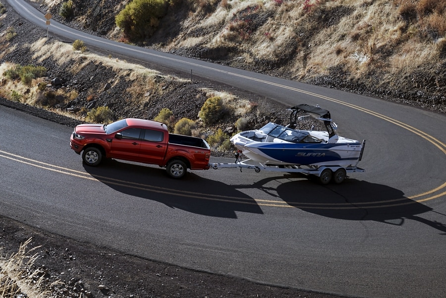 Una Ford Ranger 2023 en Hot Pepper Red Metallic Tinted Clearcoat remolcando un bote en una carretera sinuosa