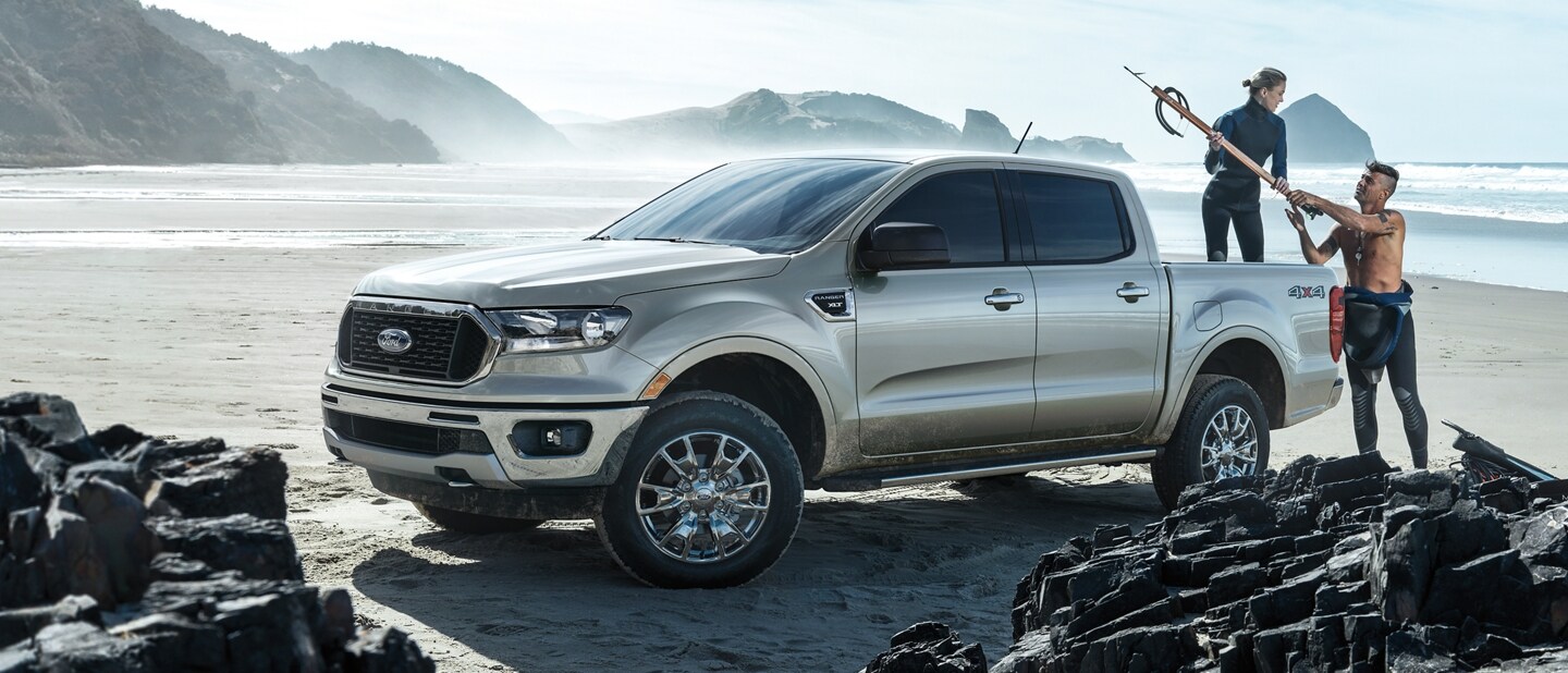 2023 Ford Ranger parked on a rocky beach with surfers loading gear into the box