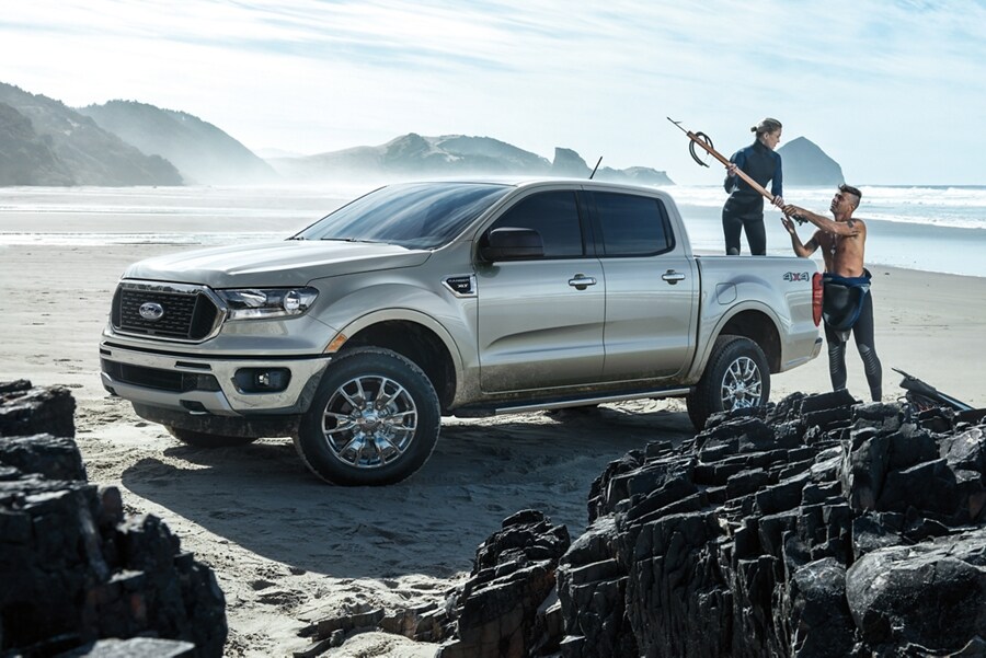 Una Ford Ranger 2023 en una playa rocosa con surfistas cargando equipos en la plataforma