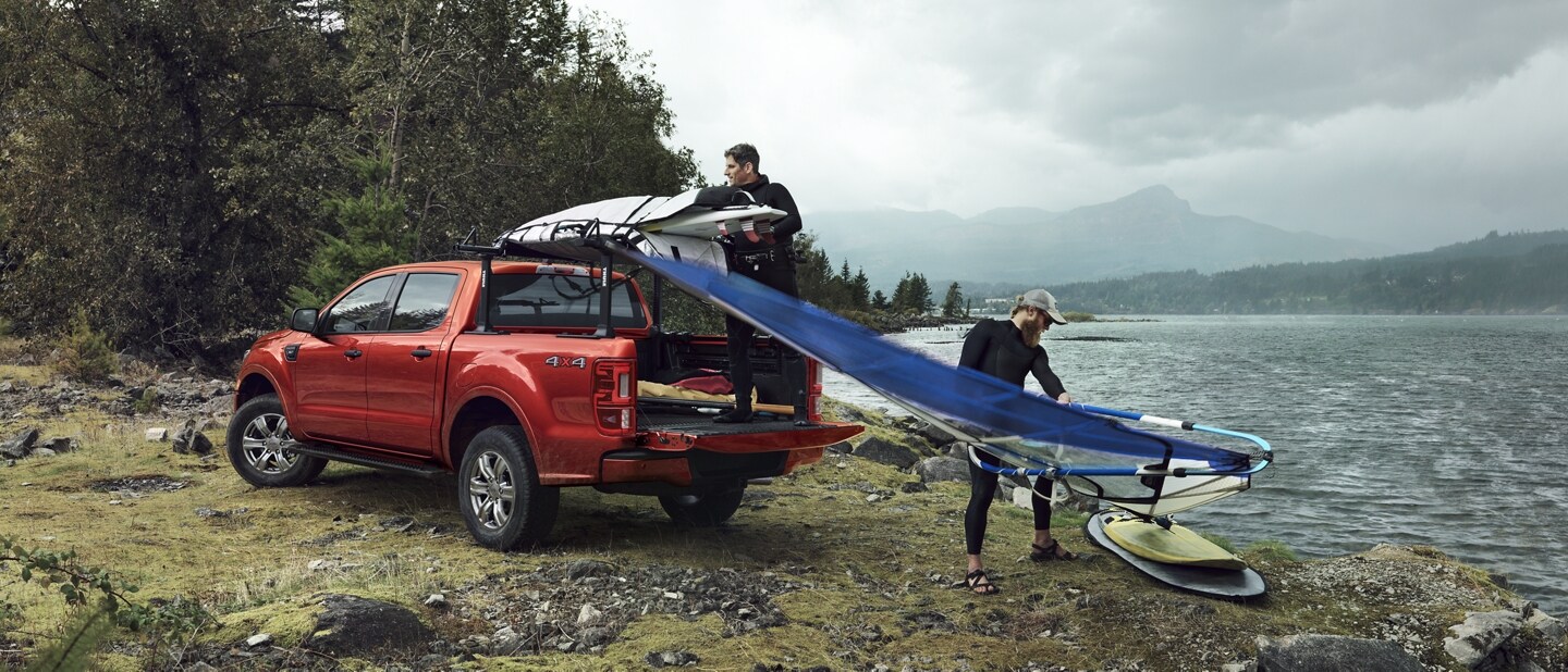 Una Ford Ranger 2023 en Hot Pepper Red estacionada cerca de un lago con personas practicando windsurf