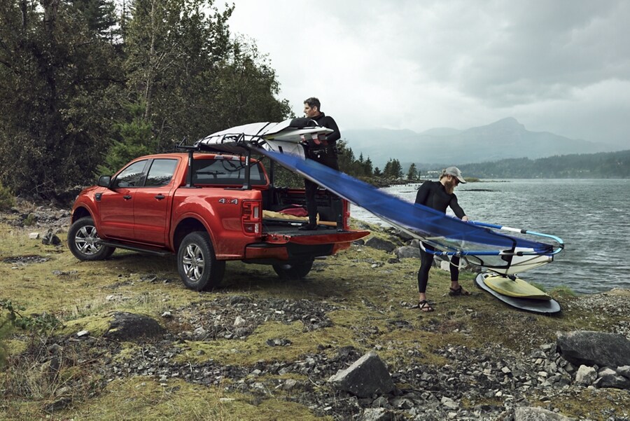 Una Ford Ranger 2023 en Hot Pepper Red estacionada cerca de un lago con personas practicando windsurf