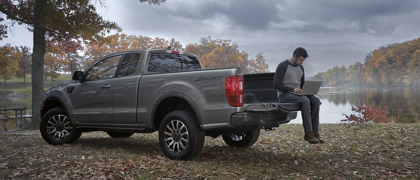 Se muestra una Ford Ranger® SuperCab sport 2023 en carbonized gray con un hombre usando una laptop sobre la puerta trasera