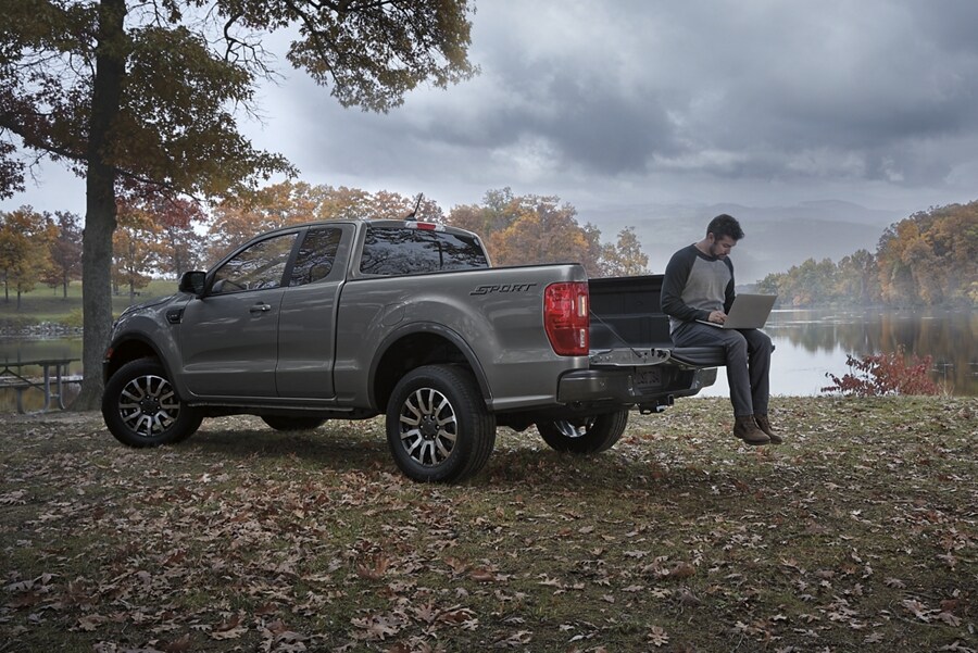 Una Ford Ranger® 2023 en Carbonized Gray estacionada cerca de un lago, y un hombre sentado en la puerta trasera