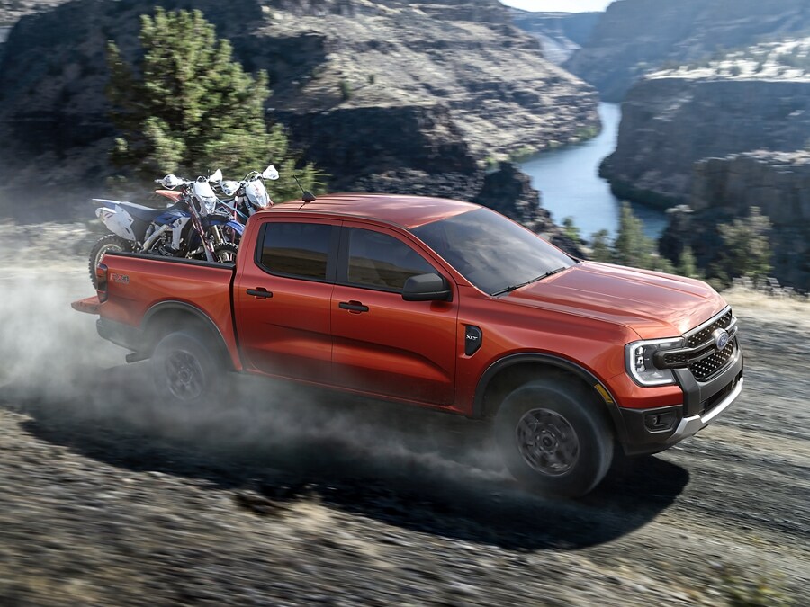 A 2024 Ford Ranger® in Hot Pepper Red hauls dirt bikes in the bed along a ravine
