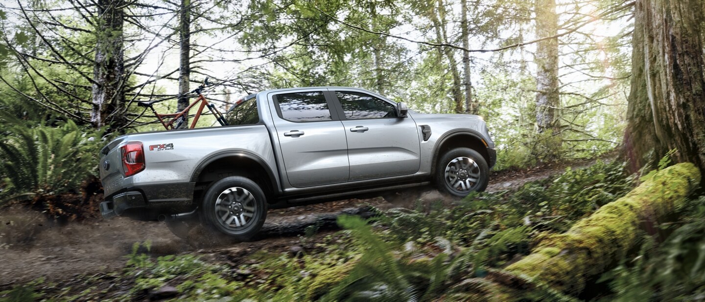 A 2024 Ford Ranger® truck in Iconic Silver Metallic is being driven off-road in a scenic location with trees