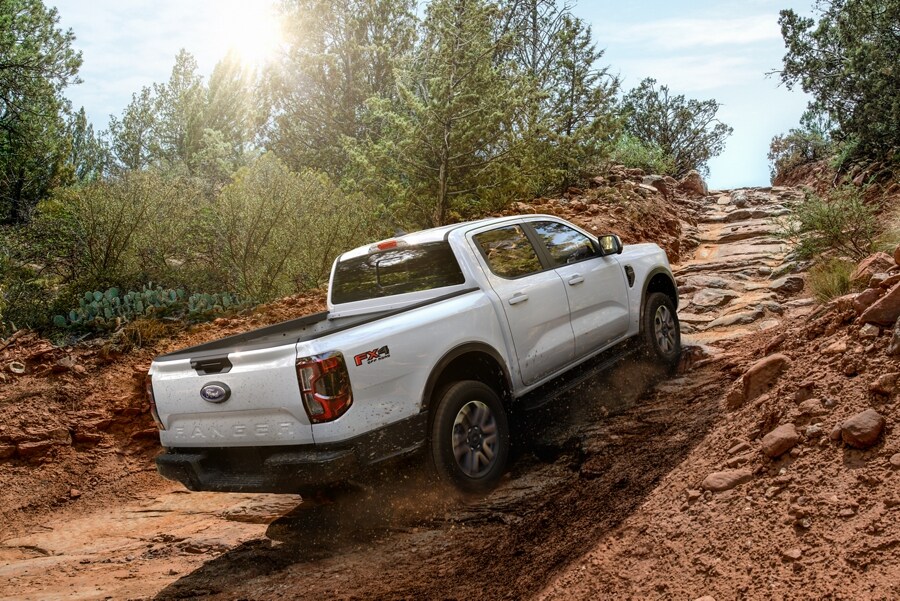 A 2024 Ford Ranger® truck in Oxford White is being driven on rocky terrain with secured bikes in the truck bed