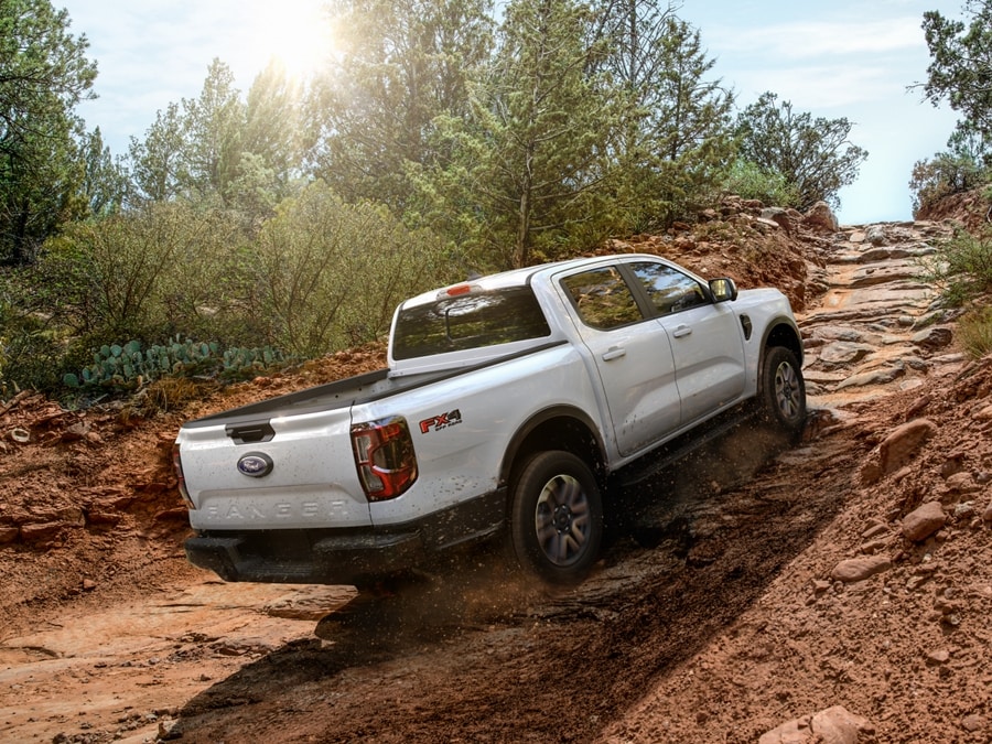 A 2024 Ford Ranger® in Oxford White is being driven up a trail with mountain bikes mounted in the truck bed
