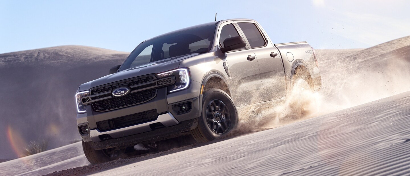 A 2024 Ford Ranger® Raptor® in Iconic Silver is accelerating on a sand dune