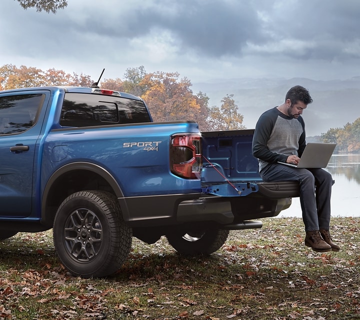 A person with a laptop in the bed of a 2024 Ford Ranger® in a scenic location