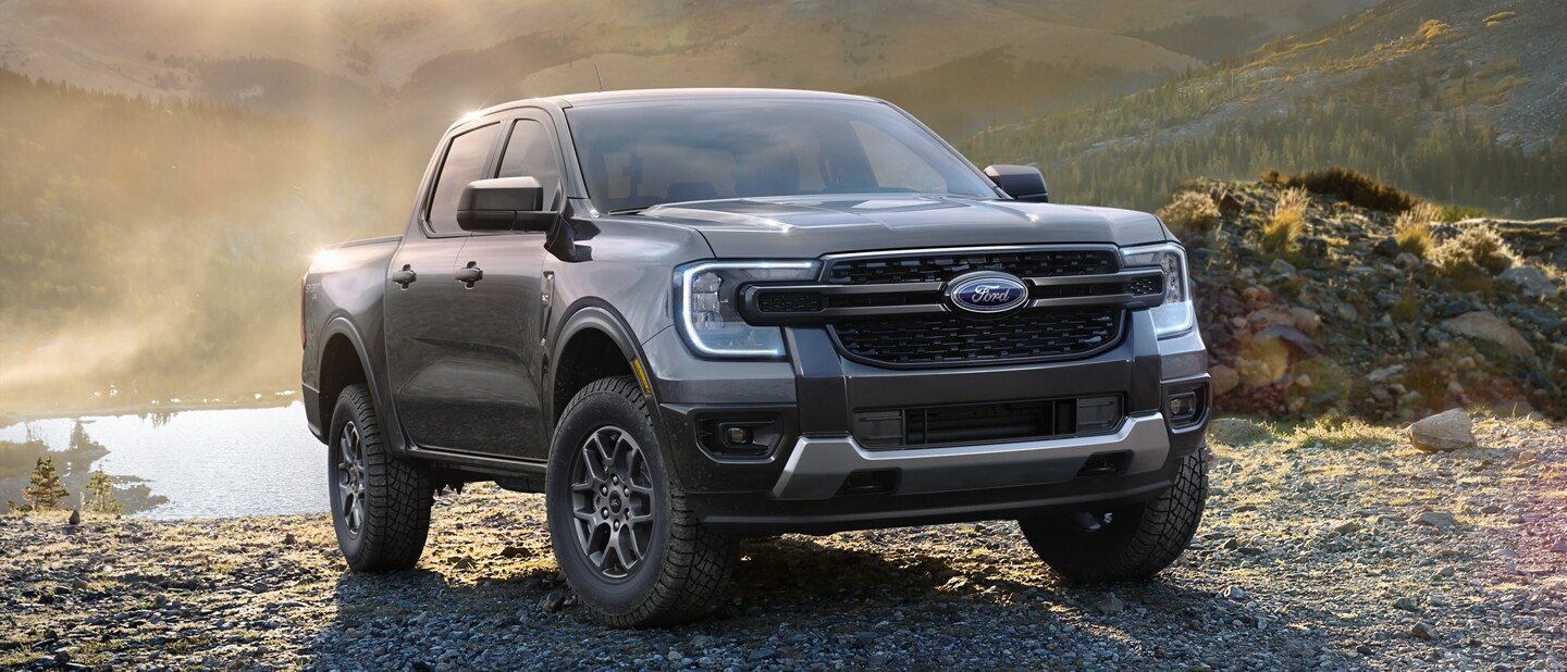 A 2024 Ford Ranger® is parked on a dirt road in a scenic location near a lake with the sun behind it