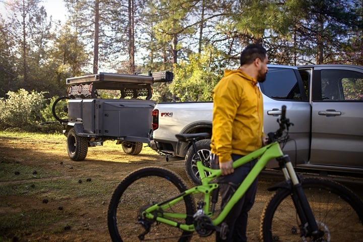 A 2024 Ford Ranger® LARIAT® truck with a trailer next to a person with a bike in a scenic location
