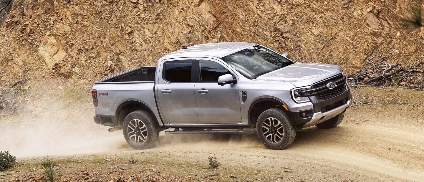 A 2024 Ford Ranger® truck in Velocity Blue is being driven on a dirt road near mountain terrain