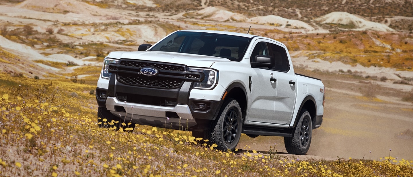 A 2024 Ford Ranger® truck in Oxford White is being driven up a hill with flowers in a scenic location