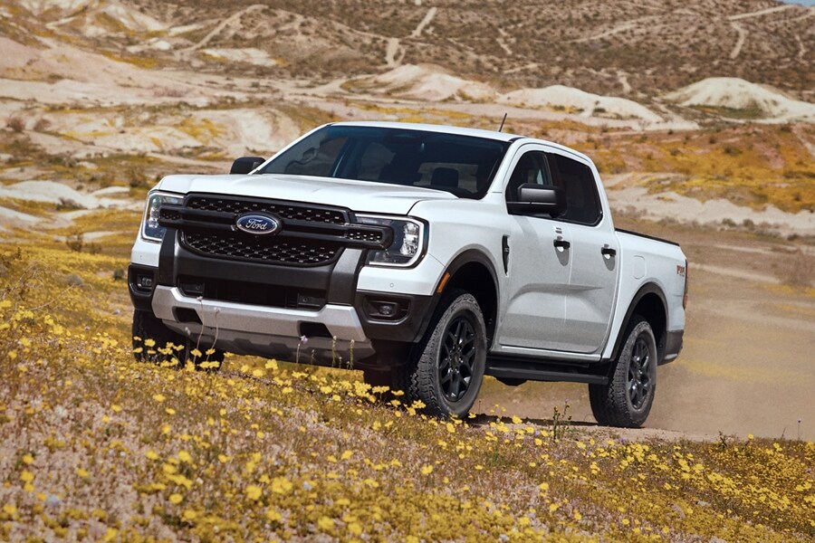 A 2024 white Ford Ranger® is being driven up a sandy hill in a scenic location 