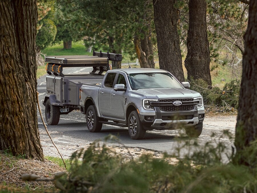 A 2024 Ford Ranger® in Cactus Gray tows a trailer along a wooded road
