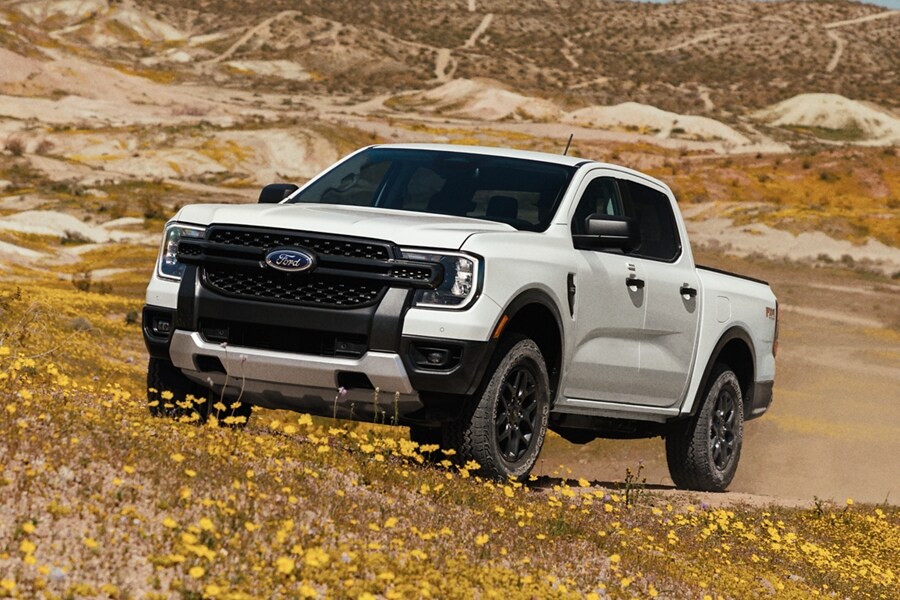A 2024 Ford Ranger® in Oxford White is being driven up a sandy hill in a scenic location