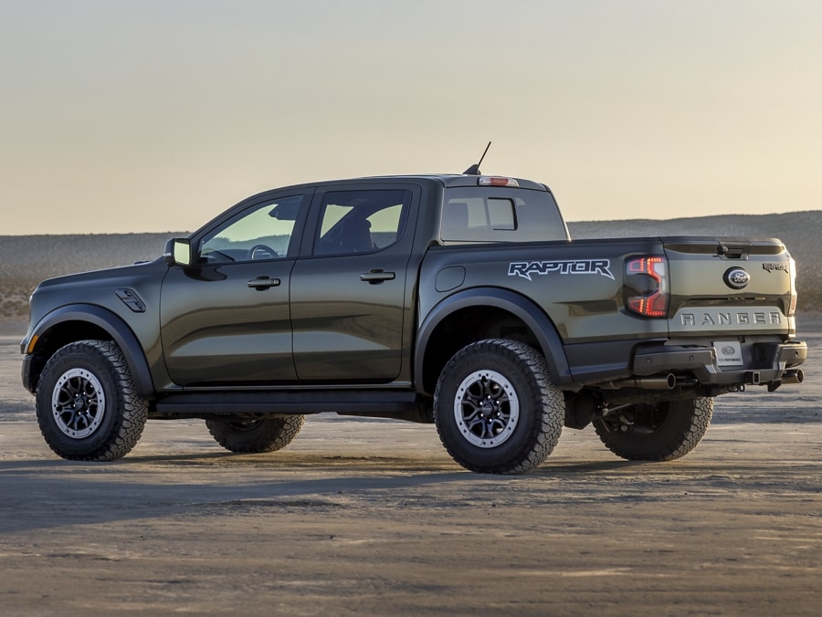 A 2024 Ranger® Raptor® in Shelter Green is being driven on a sandy hill