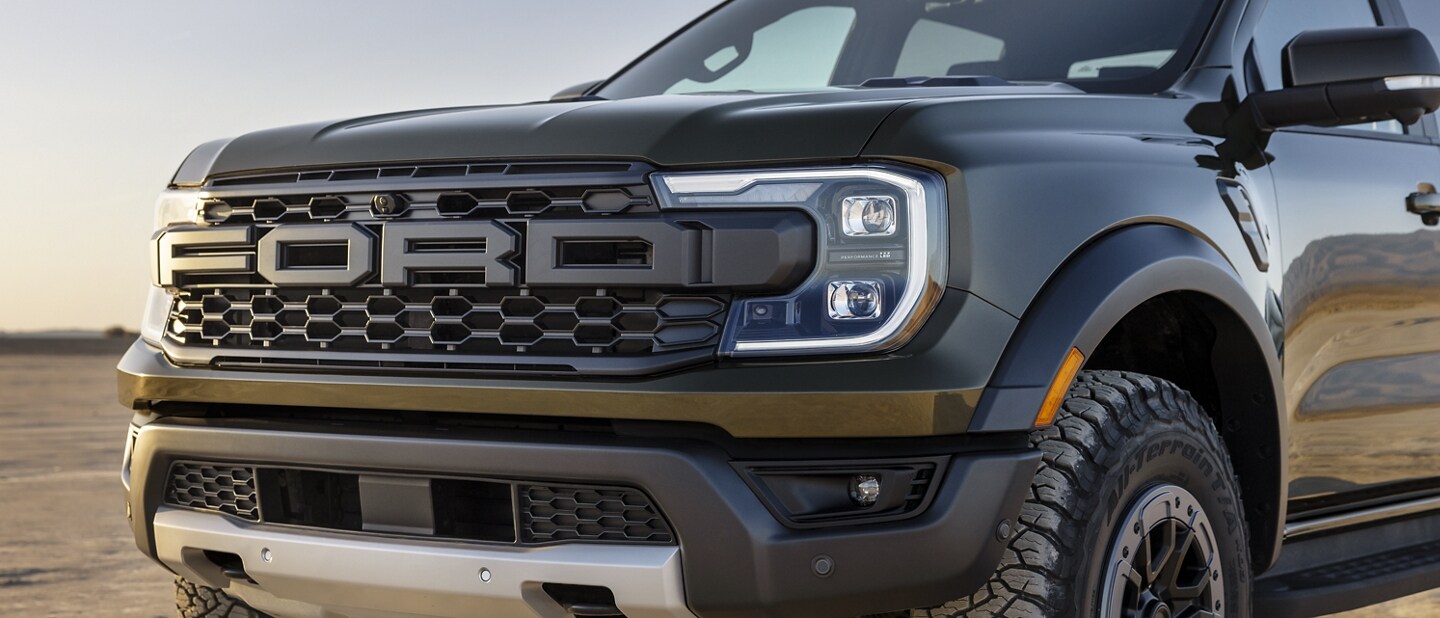 A close-up of a 2024 Ford Ranger® Raptor® parked on a dirt road with a close-up of the grille