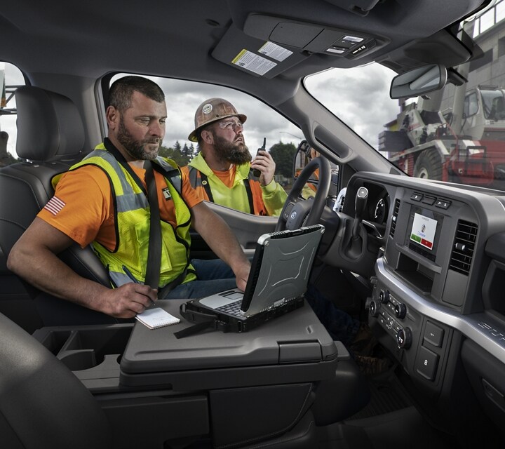 Man working on laptop inside a 2023 Ford Super Duty® F-250® XL with a worker in background