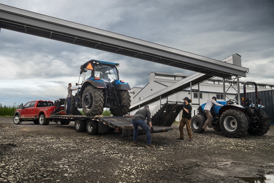 Un hombre cargando un tractor sobre un tráiler enganchado a una Ford Super Duty® F-450® XL SuperCrew®​​​​​​​ Cab 2023 cerca de una fábrica de granos