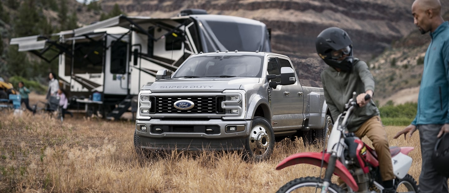 Two people in front of a 2024 Ford Super Duty® F-450® Limited Crew in Iconic Silver Metallic hitched to a camper trailer