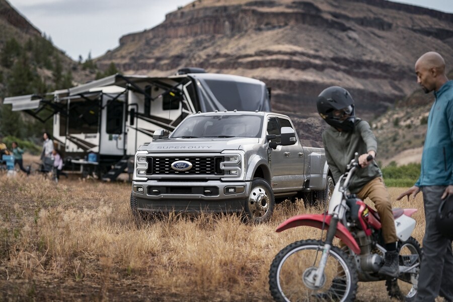 Two people in front of a 2024 Ford Super Duty® F-450® Limited Crew in Iconic Silver Metallic hitched to a camper trailer