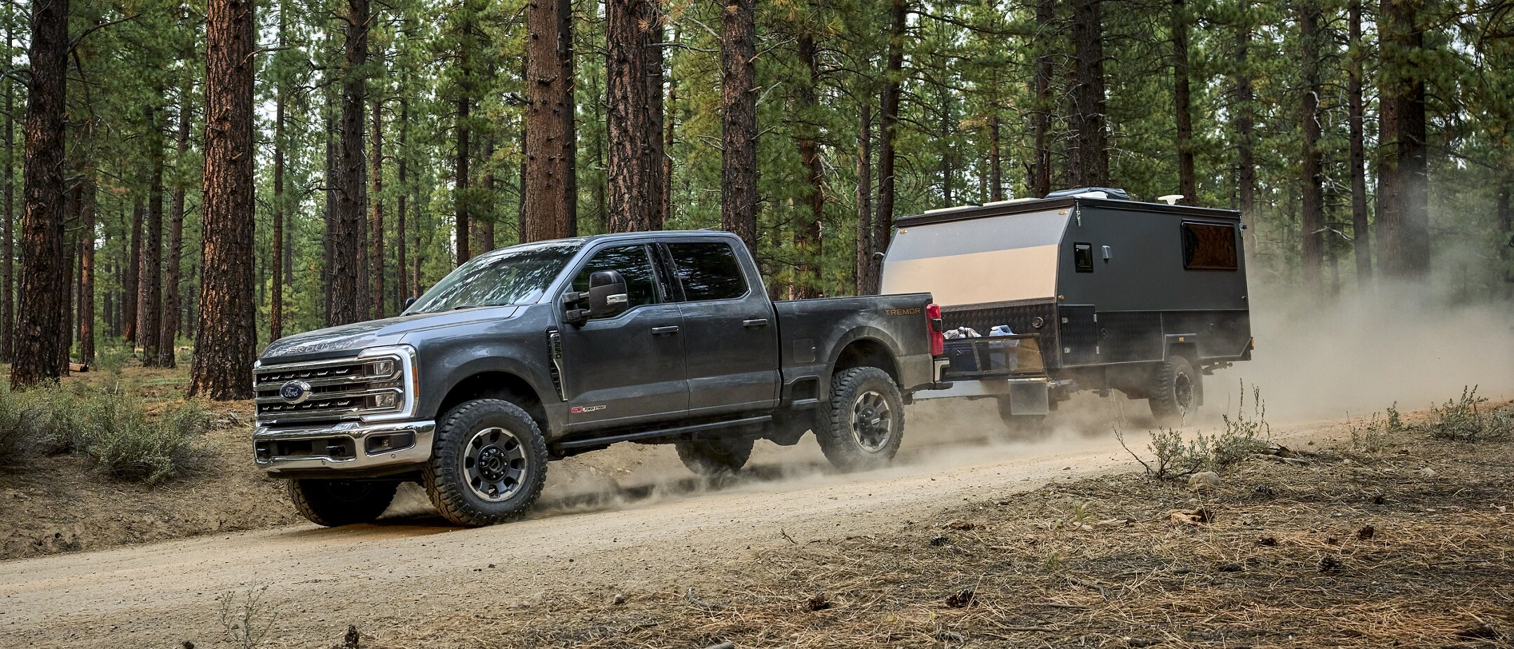 Light Blue gray 2024 F-250 Super Duty XL Off-Road Package driving off road with a small camper