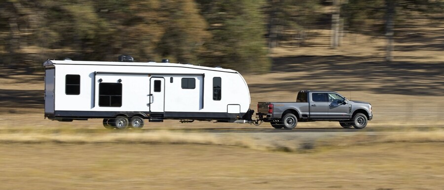 Una Ford Super Duty® F-250® 2023 con Paquete Todo Terreno Tremor remolcando una casa rodante sobre un camino de tierra