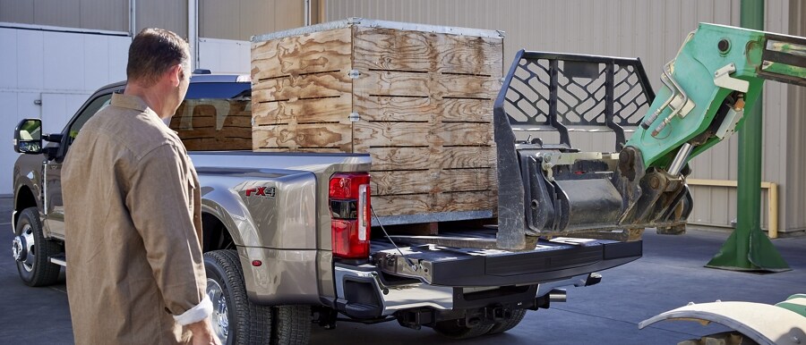 Un montacargas cargando un palé en la plataforma de una Ford Super Duty® F-350® LARIAT 2023 con un hombre junto a ella