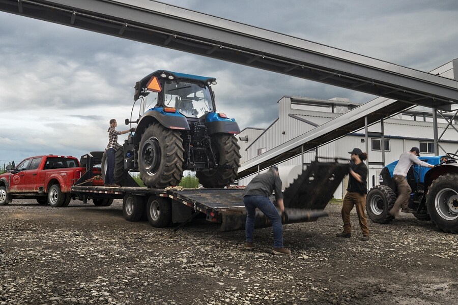 Un hombre cargando un tractor sobre un tráiler enganchado a una Ford Super Duty® F-450® XL SuperCrew®​​​​​​​ Cab 2023 cerca de una fábrica de granos