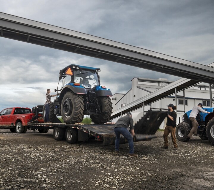 Un hombre cargando un tractor sobre un tráiler enganchado a una Ford Super Duty® F-450® XL SuperCrew®​​​​​​​ Cab 2023 cerca de una fábrica de granos