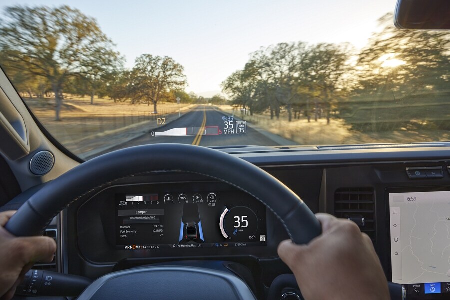 A person holding the steering wheel with the head-up display projected onto the windshield in a 2023 Ford Super Duty® pickup