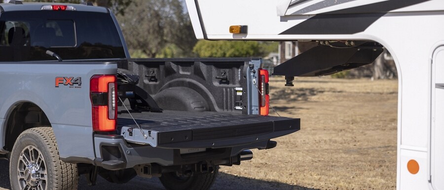 Puerta trasera abierta de una camioneta Ford Super Duty® 2023 retrocediendo hasta una caravana de 5 ruedas