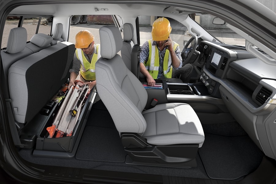 Two men working inside of a 2024 Ford Super Duty® pickup with the rear seat lifted highlighting the under-seat cargo compartment