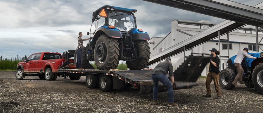 Men loading a tractor onto a trailer hitched to a 2024 Ford Super Duty® F-450® XL SuperCrew® Cab near a grain factory