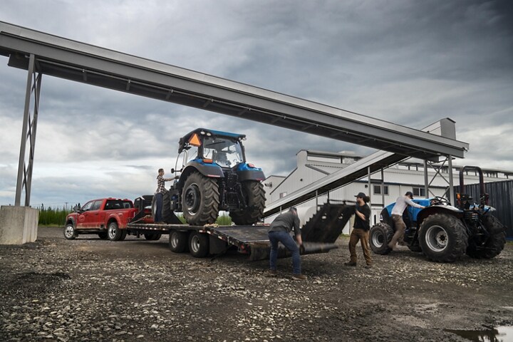 Men loading a tractor onto a trailer hitched to a 2024 Ford Super Duty® F-450® XL SuperCrew® Cab near a grain factory