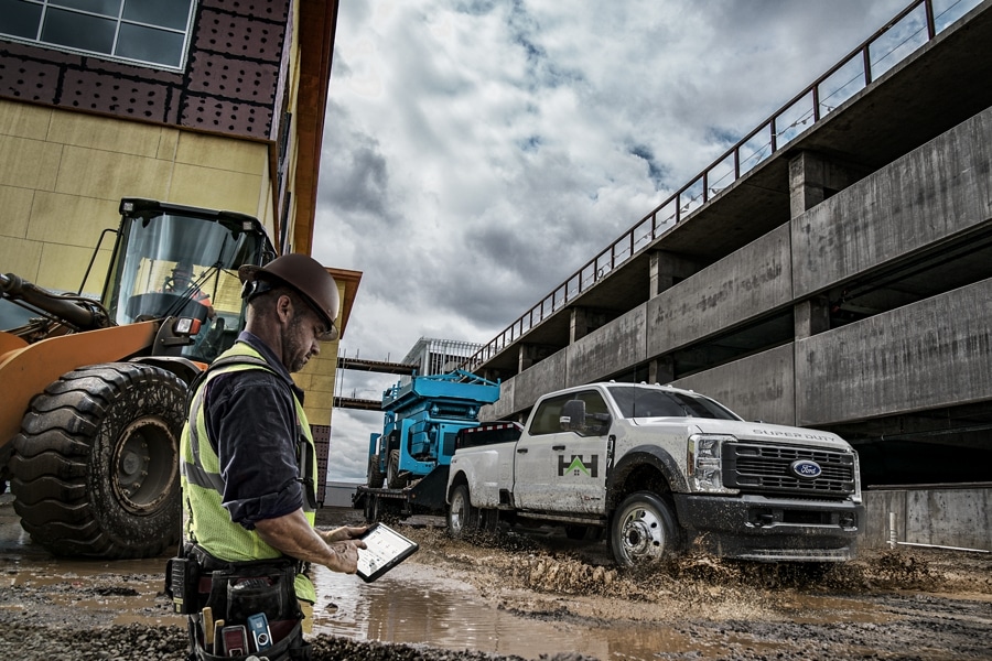 Man using a tablet while a 2024 Ford Super Duty® F-450® SuperCrew® Cab pulls a hydraulic lift on a trailer through muddy water